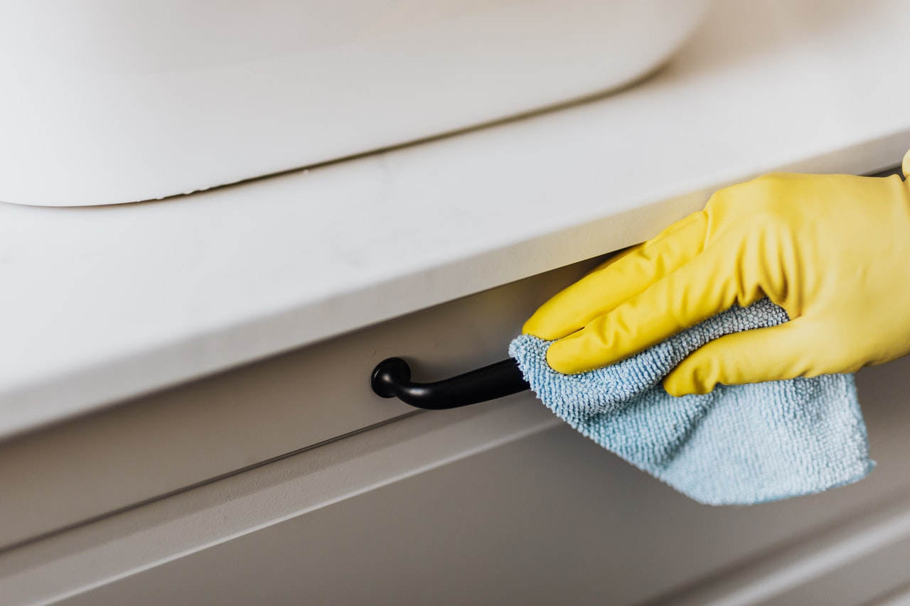 Person cleaning cabinet handle with a rag